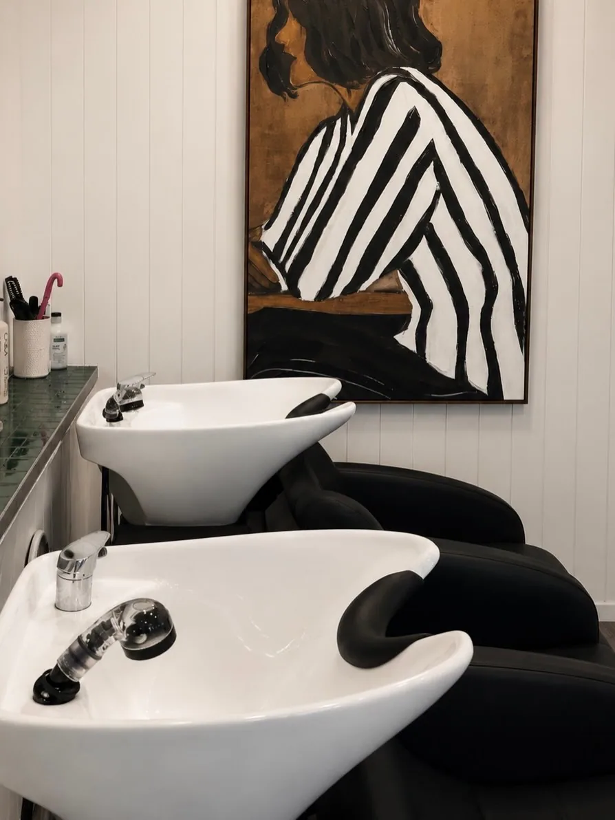 The basins at Fitzgerald Co. Salon, under a painting of a woman in a striped shirt